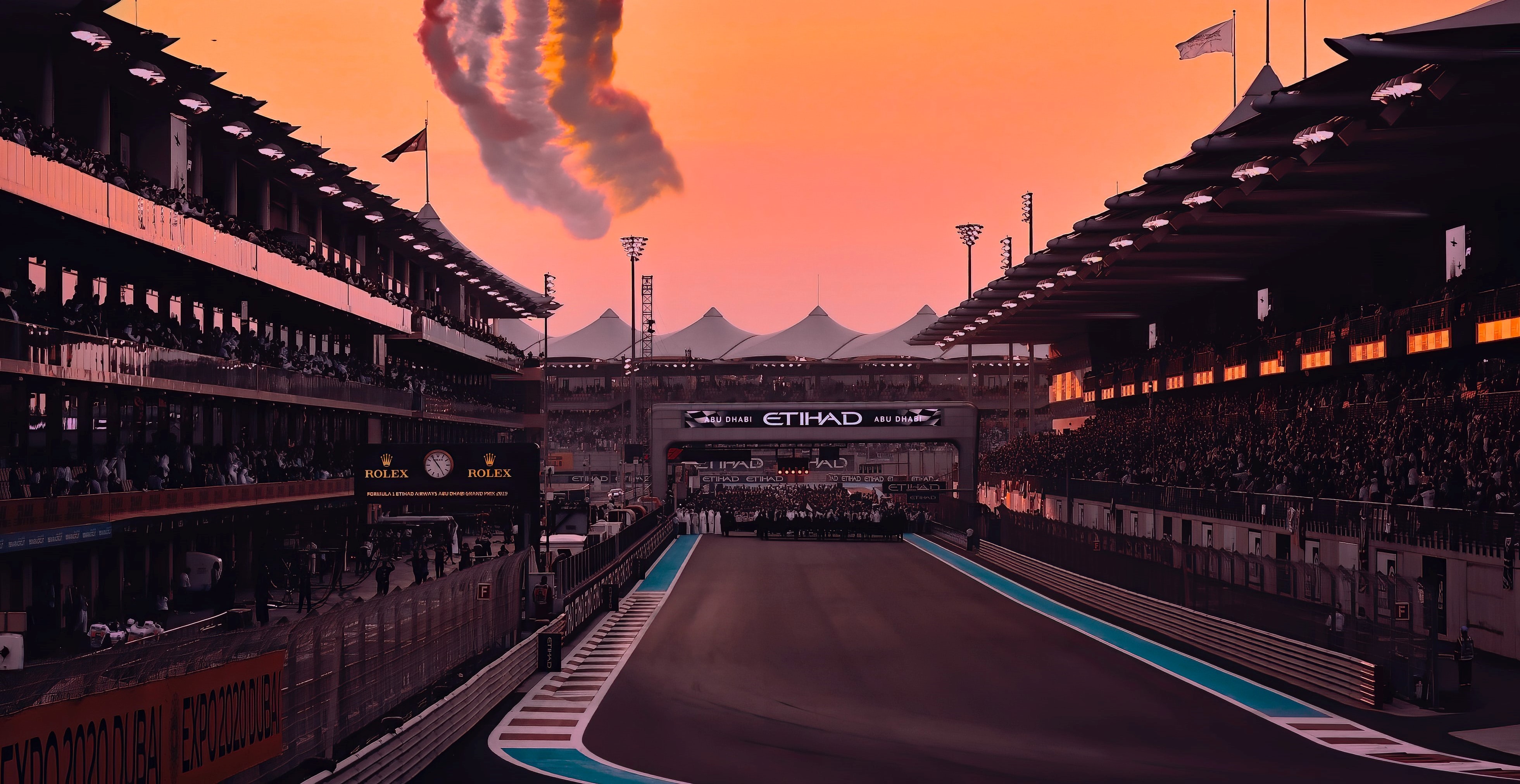 Race circuit view on finish straight with the pit lane on the left and fans on the right. Many people stand on the track in the distance.